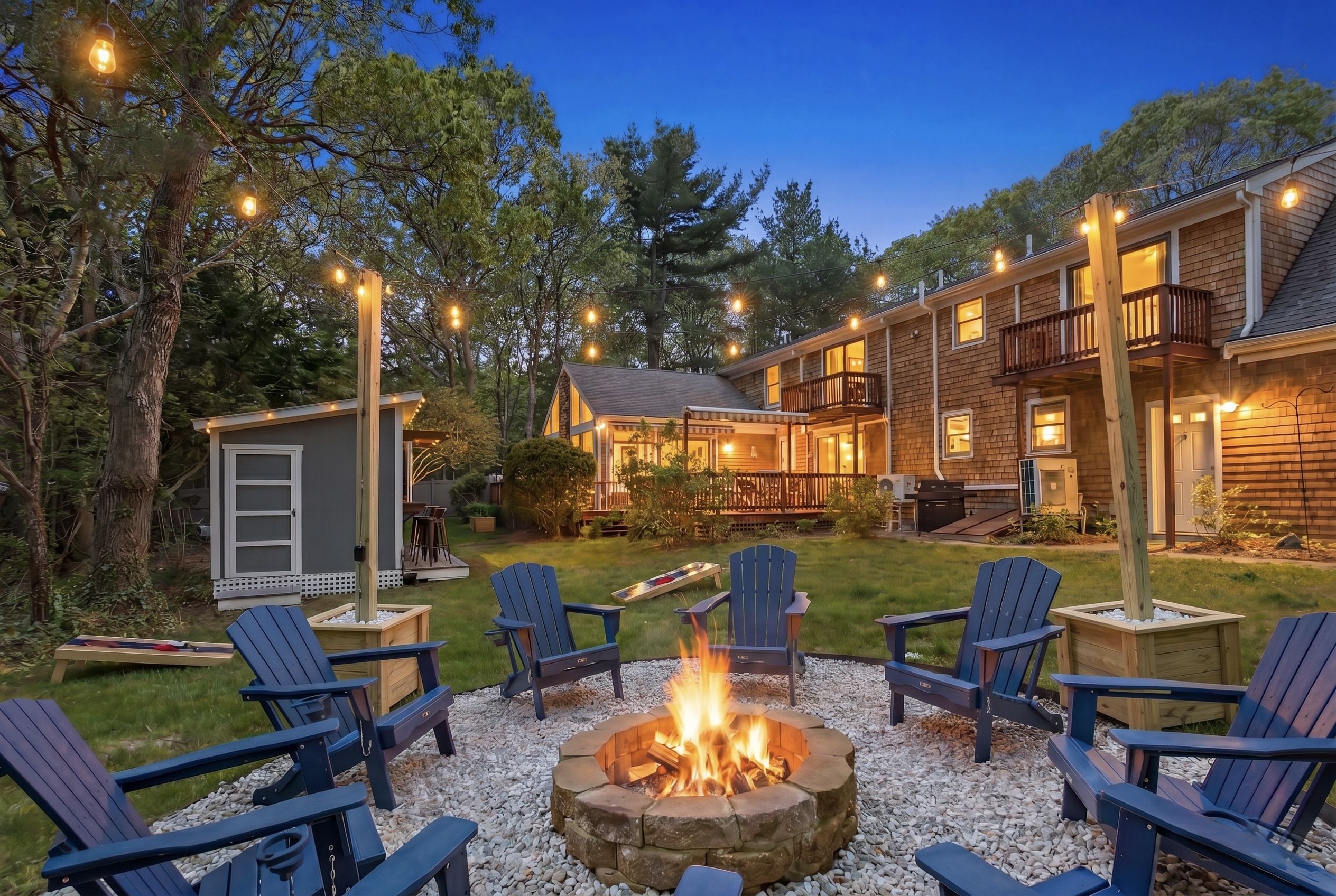 Fenced backyard with a fire pit and string lights glowing at twilight