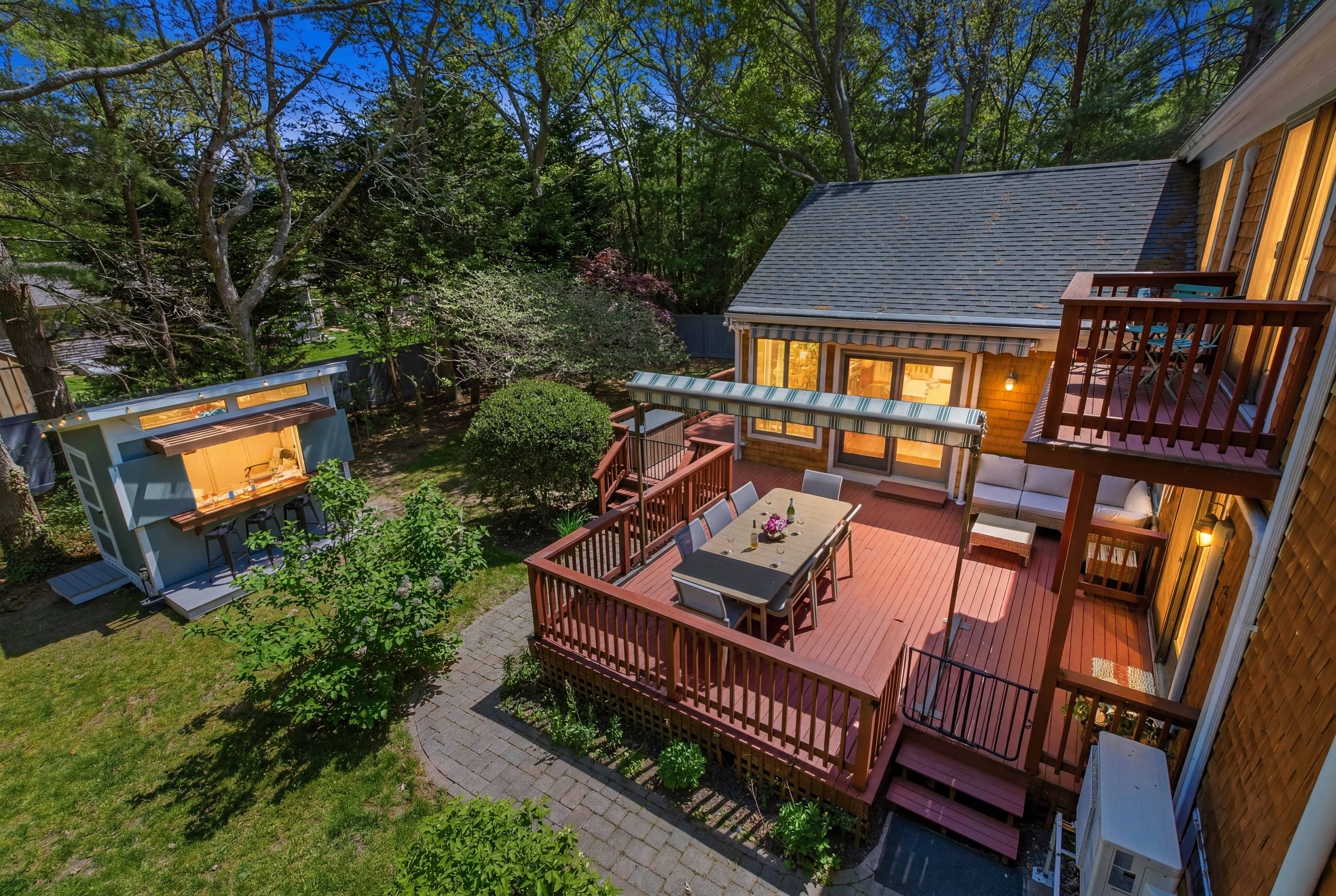 Elevated twilight view of the deck set for dinner with wine and a wicker sectional beneath the awning, the bar shed and balconies lit up beside it