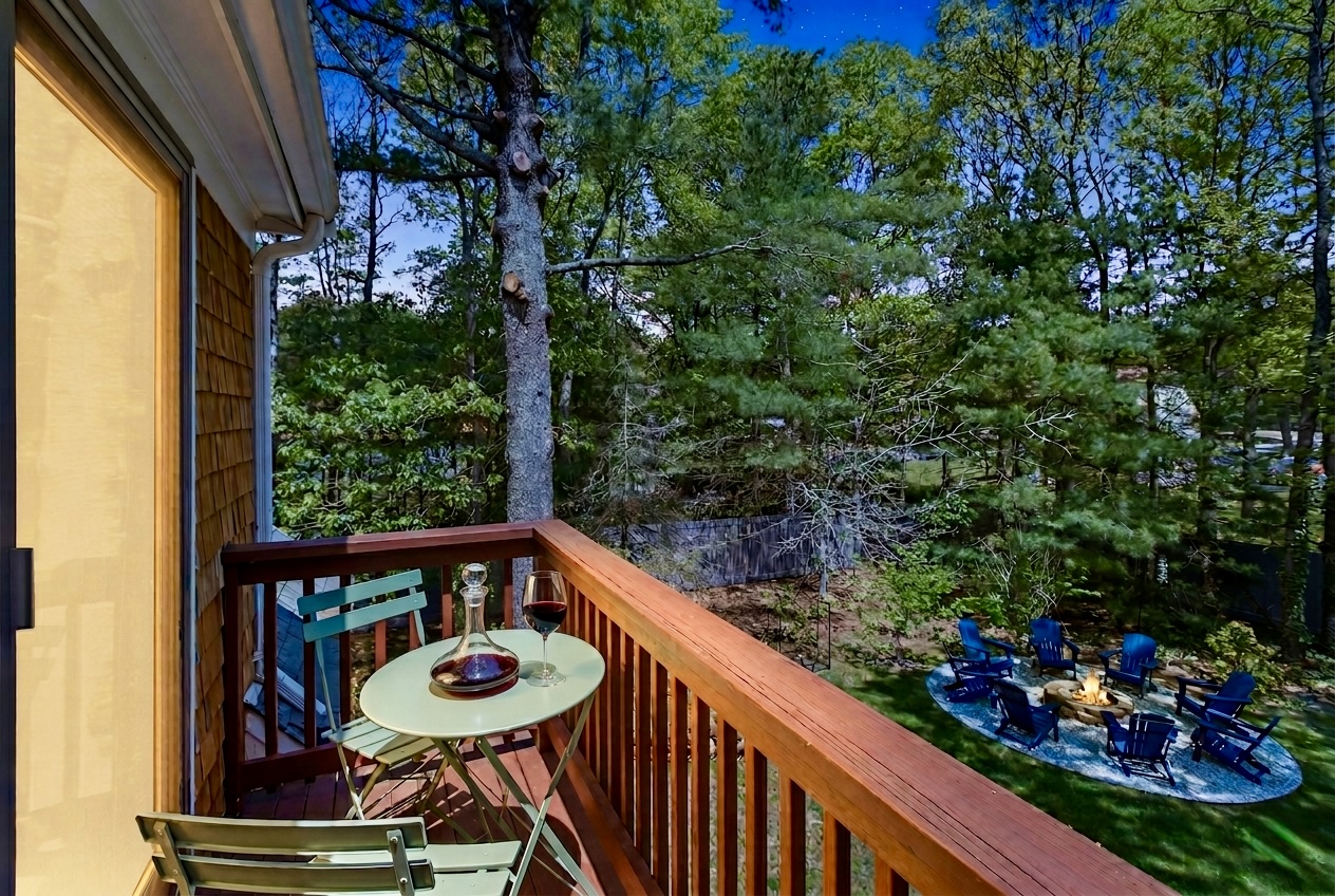Private balcony at twilight with a green bistro table, a decanter and glass of red wine, overlooking the fire-pit lounge glowing below under a starlit sky