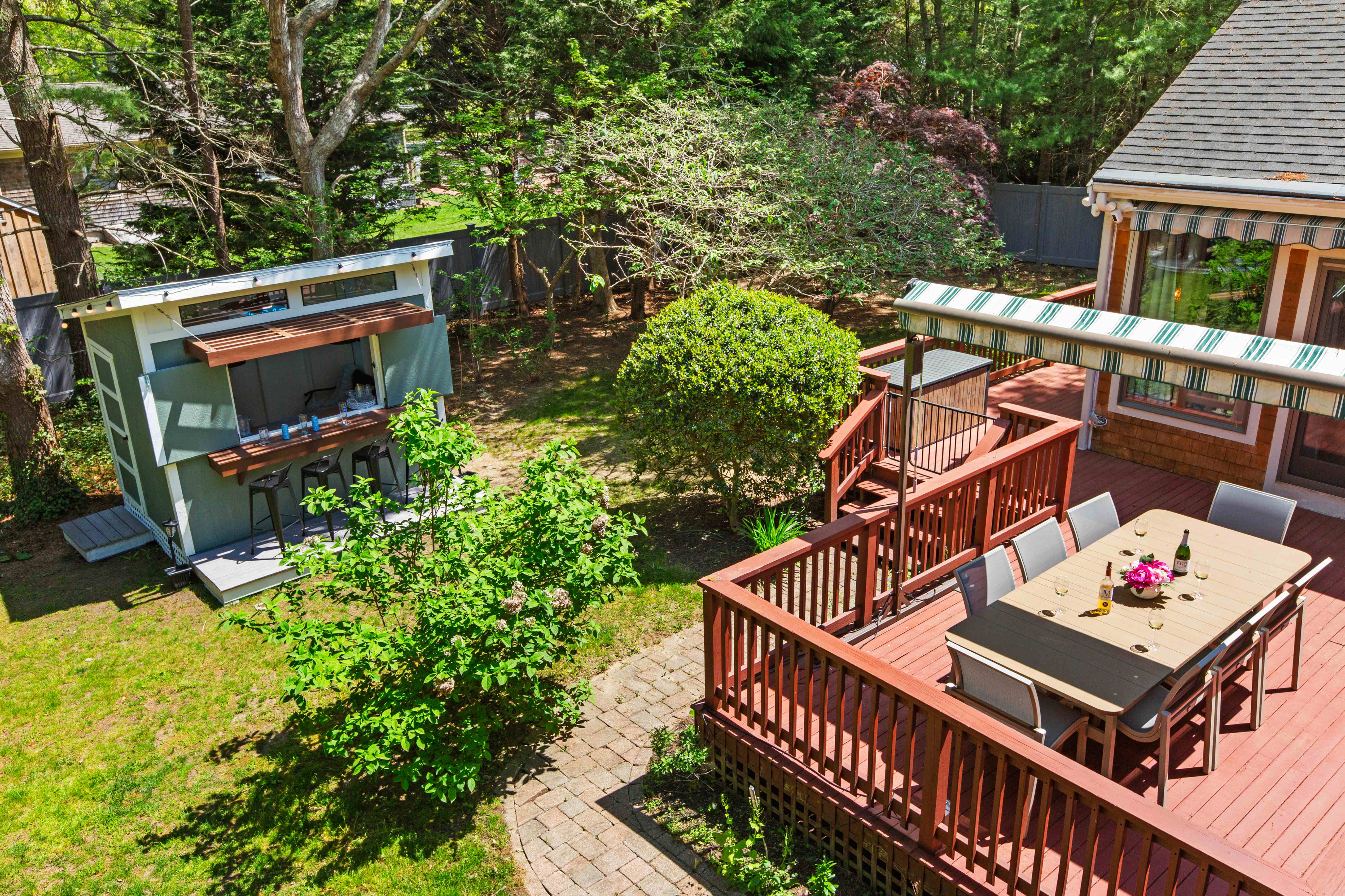 Aerial view of the raised deck dining table under a striped awning beside the bar shed and landscaped lawn