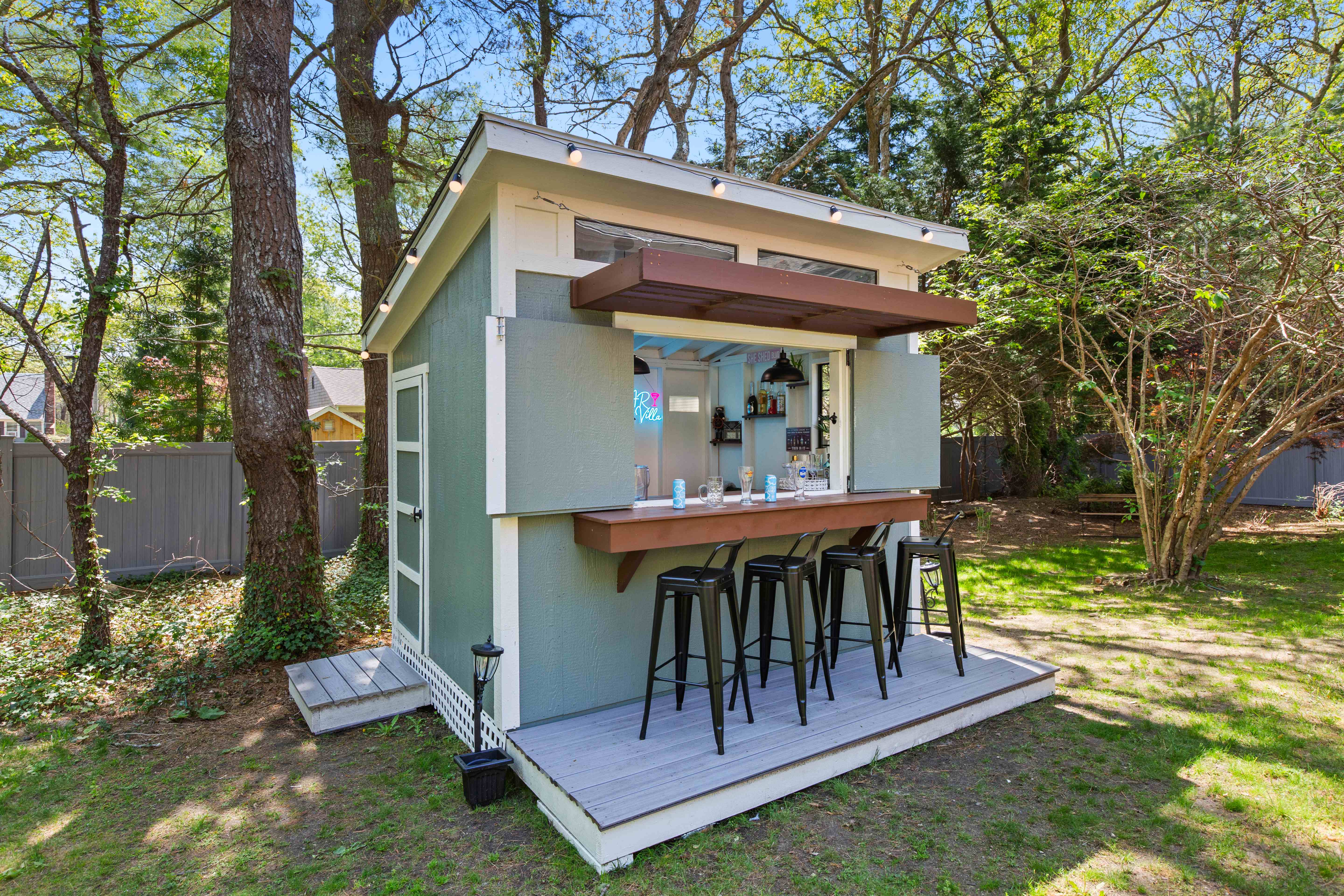 Three-quarter view of the bar shed with its deck, side door, and string lights among the trees