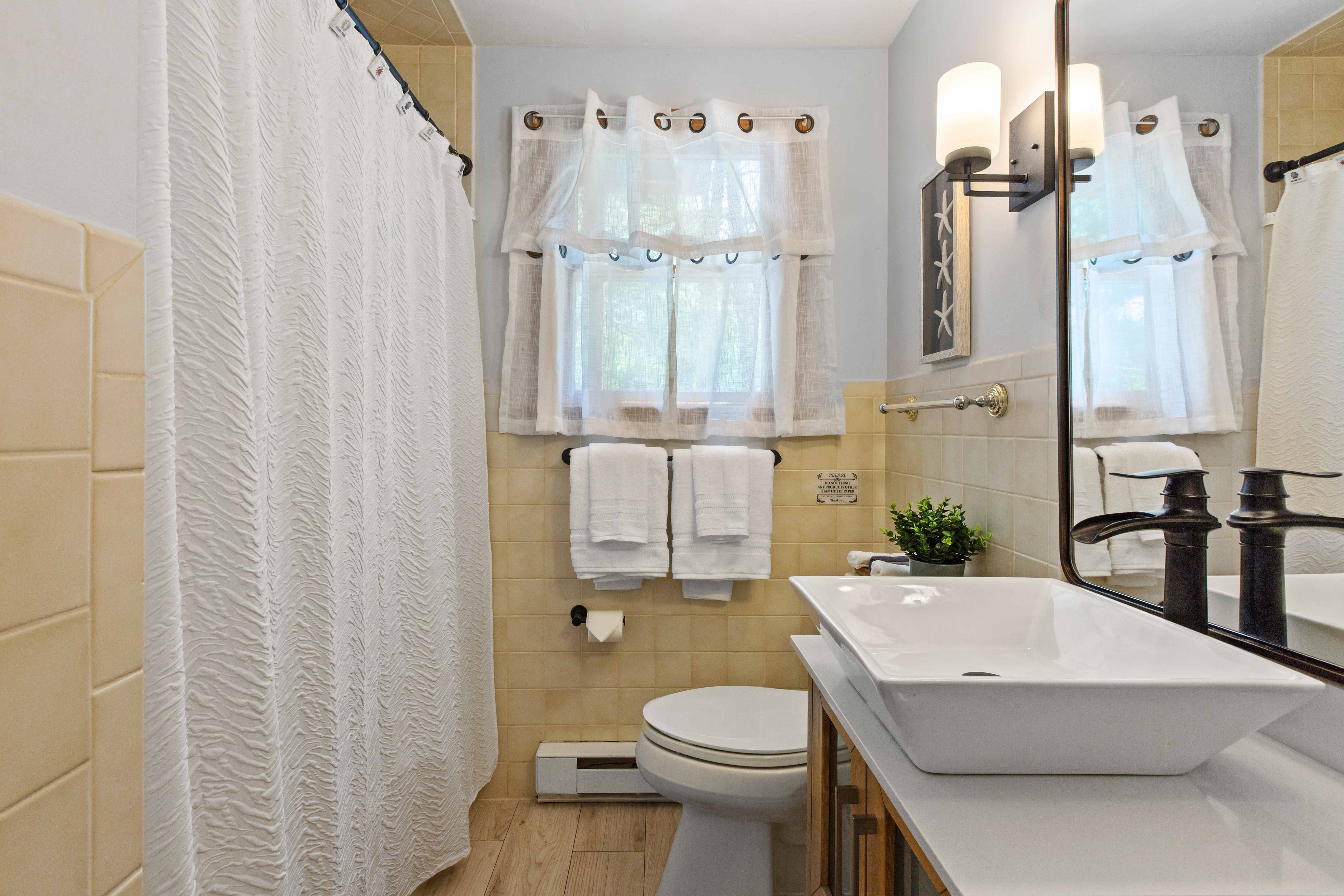 Buoy Quarters en-suite with a wood vanity, white vessel sink, bronze fixtures, and sheer cafe curtains