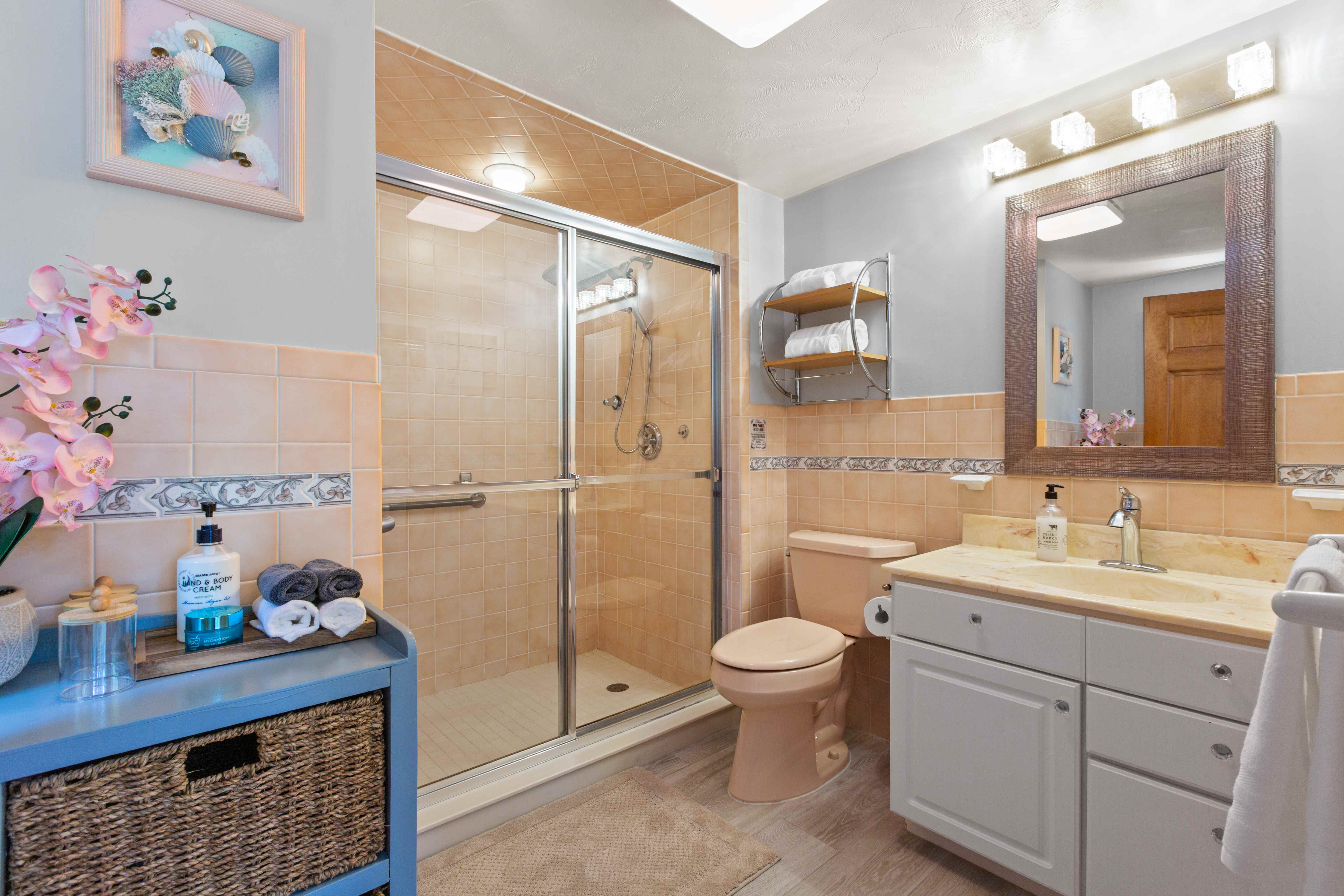 Peach-tile bathroom with a glass shower, blue console, seashell art, and orchids