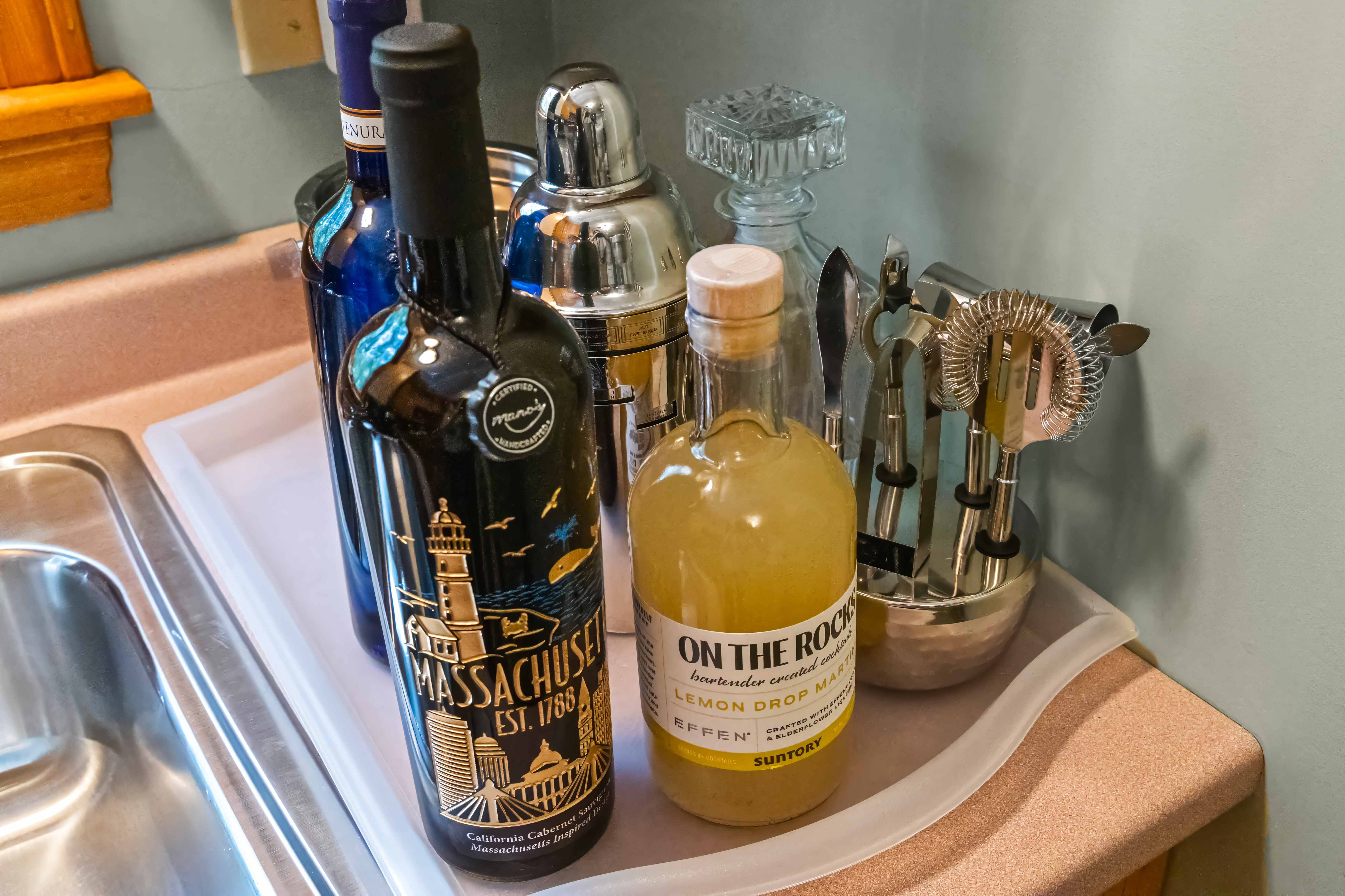 Close-up of spirits, cocktail shakers, glassware, and bar tools beside the sink