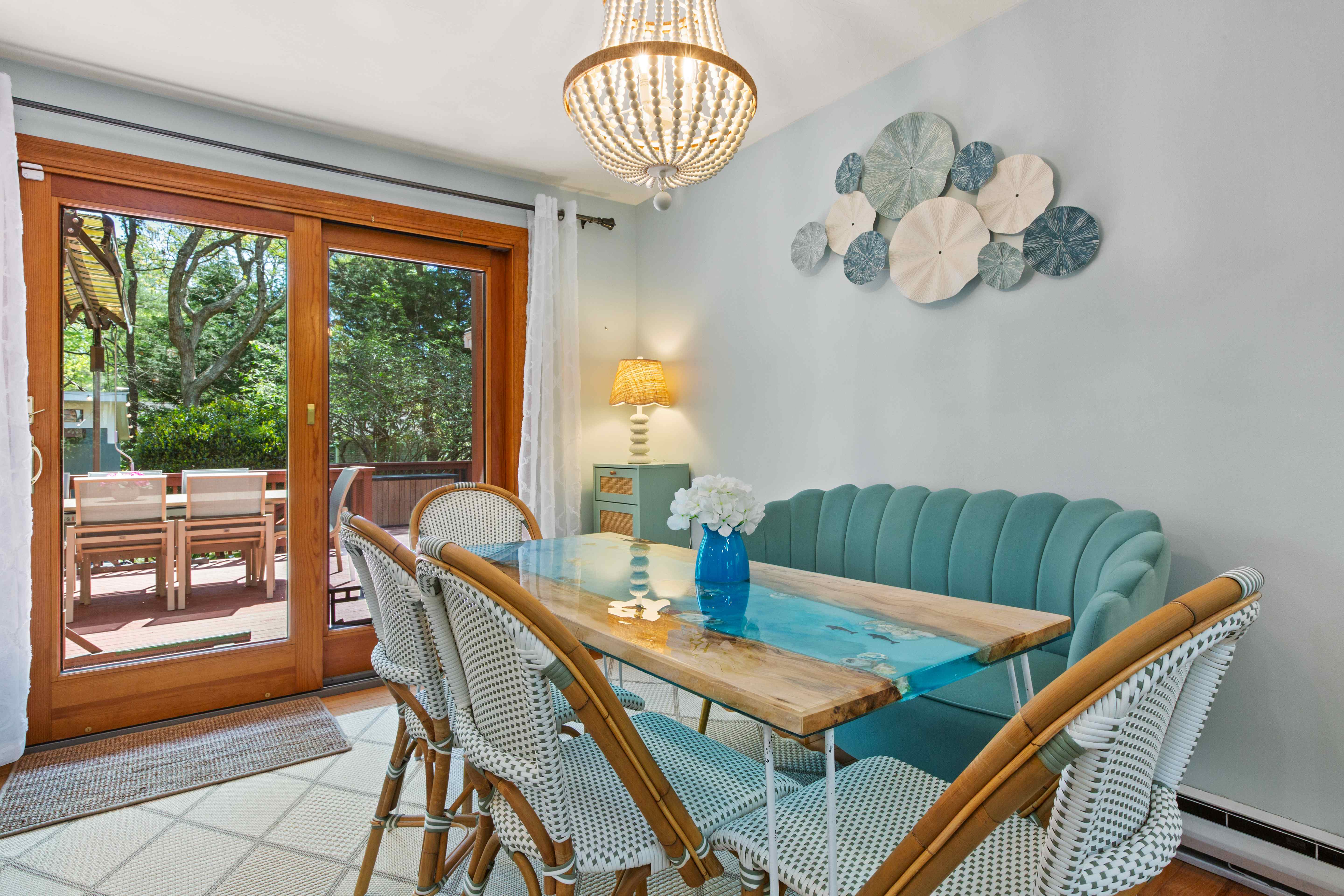 Breakfast area with a turquoise resin-and-wood dining table, woven bistro chairs, a scalloped teal banquette, and sliding doors opening to the deck