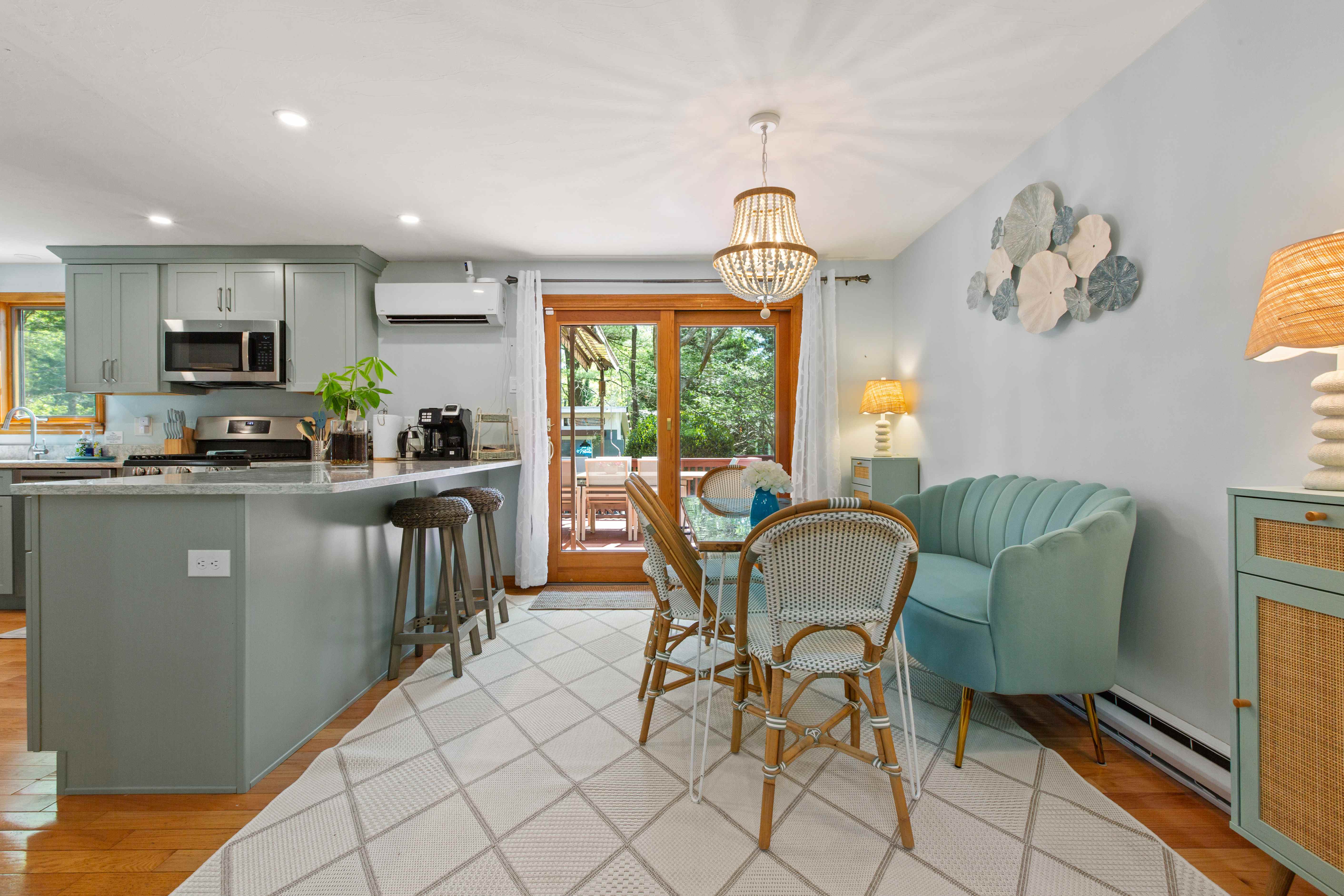 Wide view of the breakfast nook beside the sage-green kitchen, with deck access, a beaded chandelier, and a large geometric rug