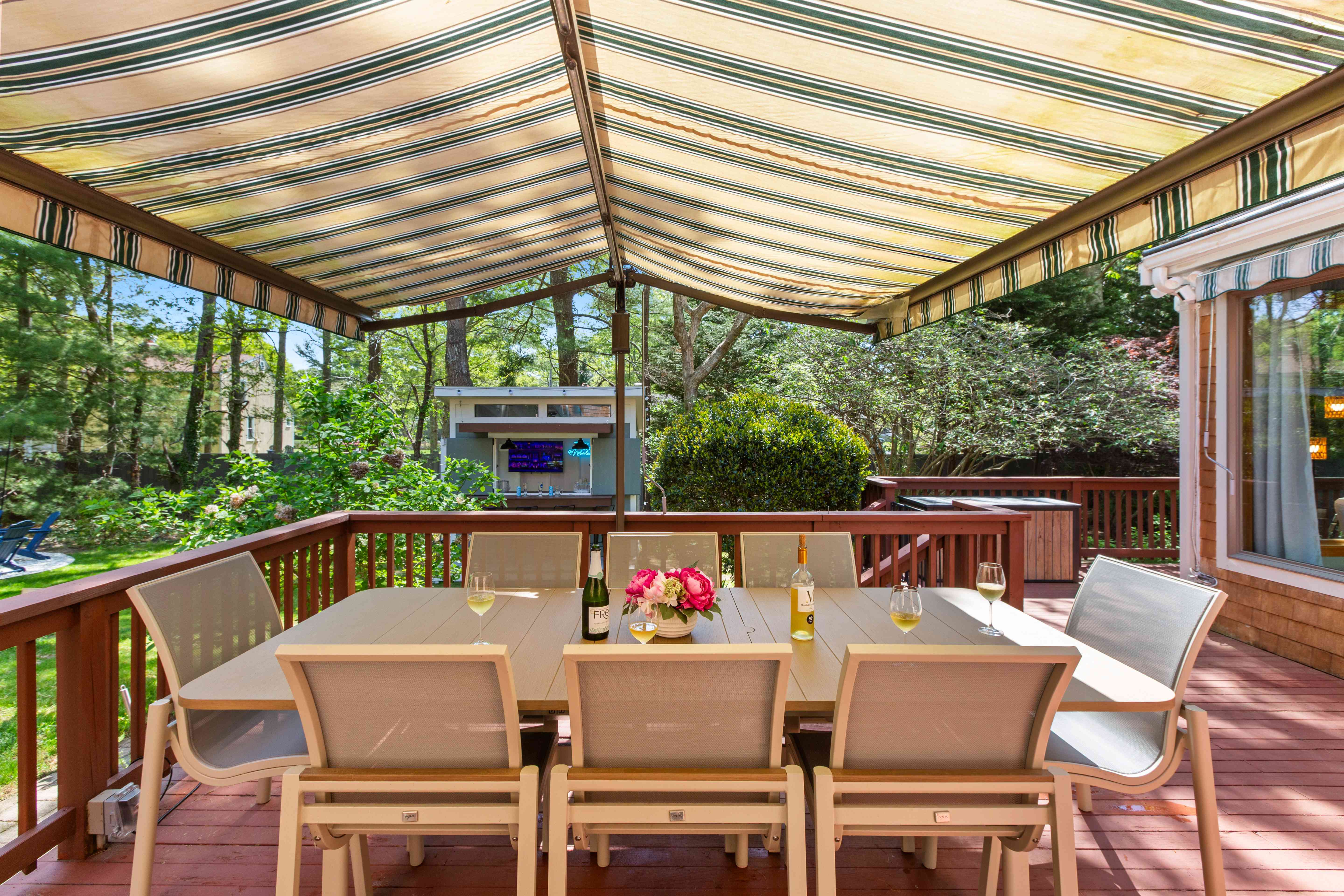 Shaded deck dining table set with wine and peonies beneath a striped retractable awning