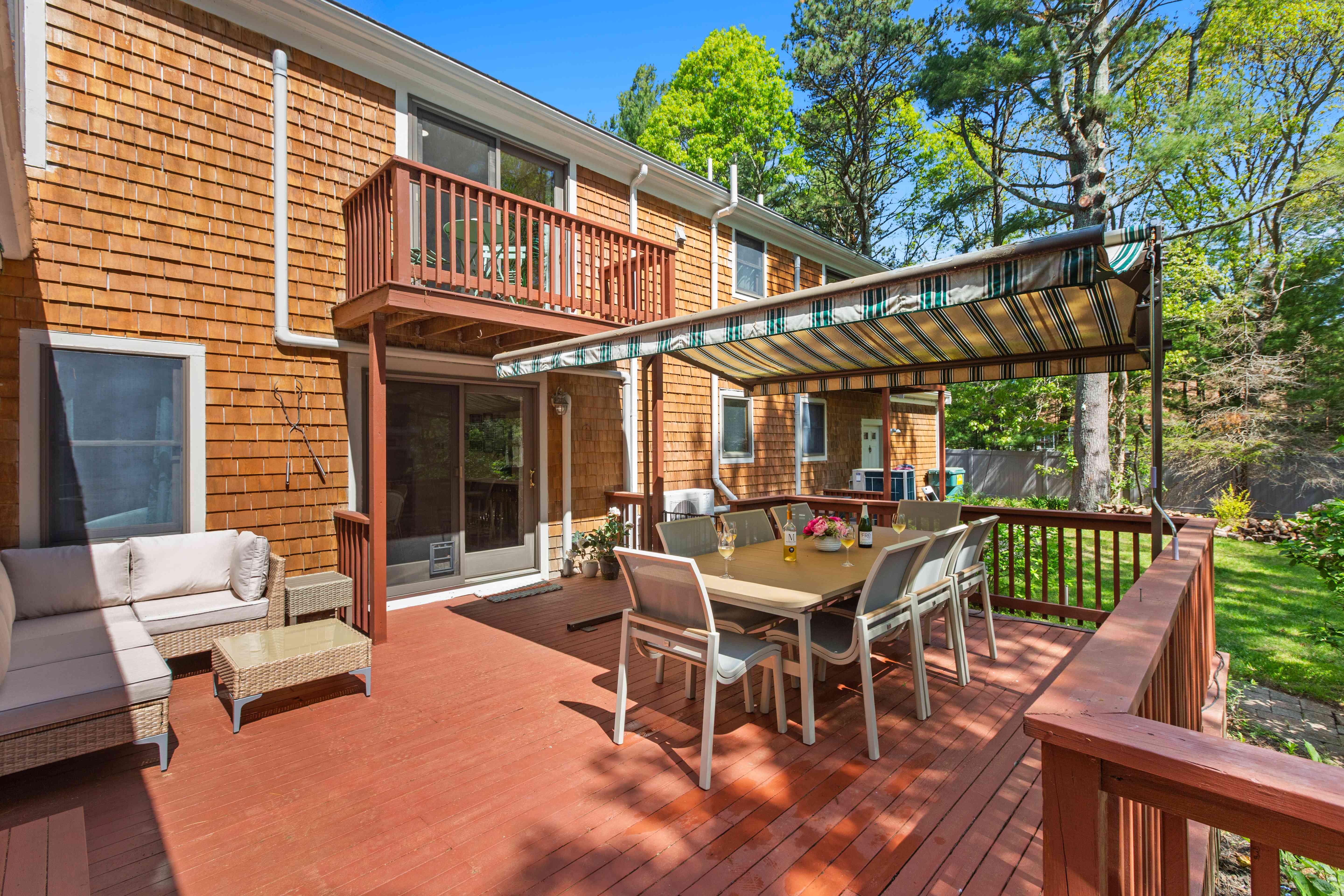 Deck with a wicker sectional lounge and dining set beside the cedar-shingled home