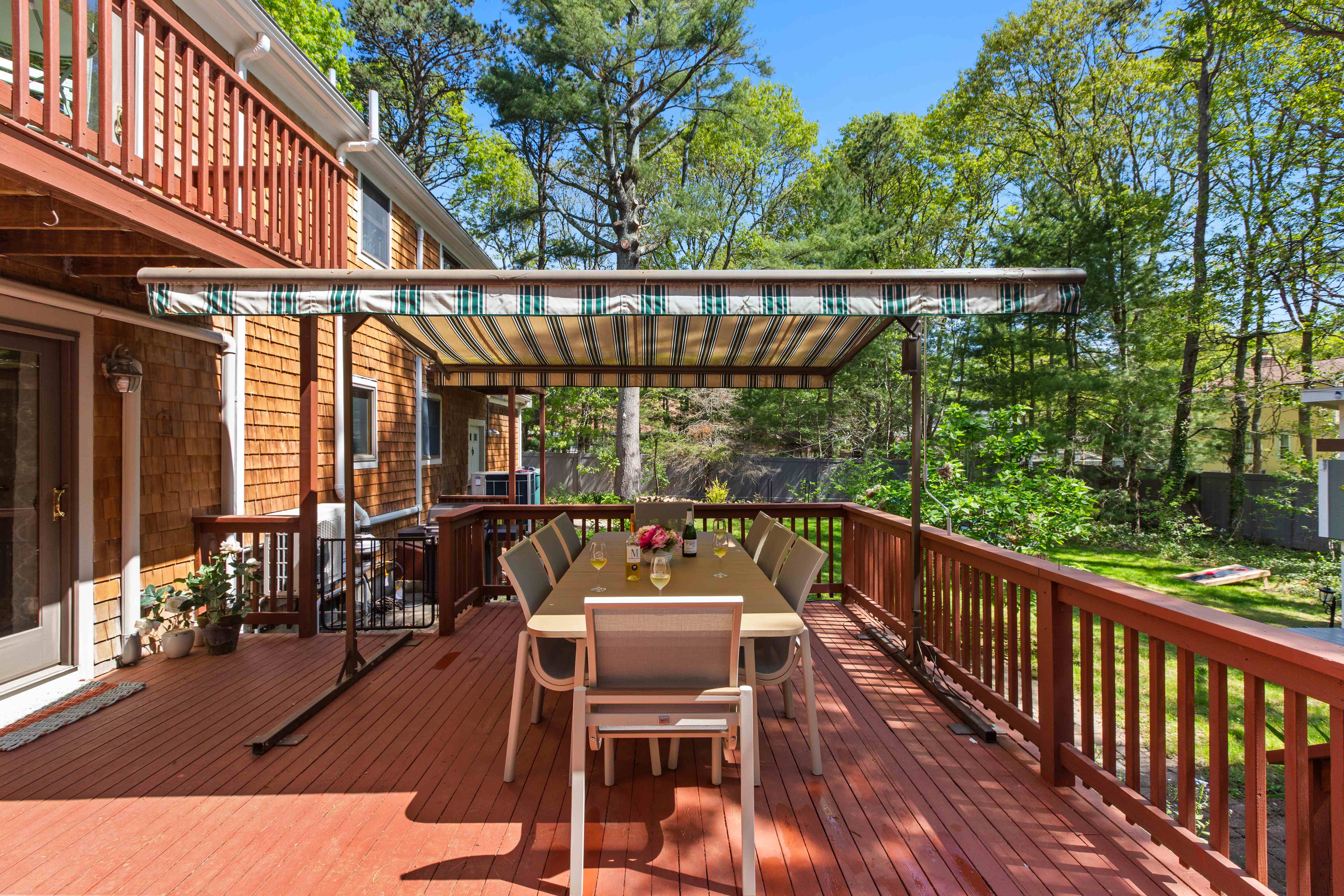 Long deck dining table beneath the awning with views into the wooded backyard