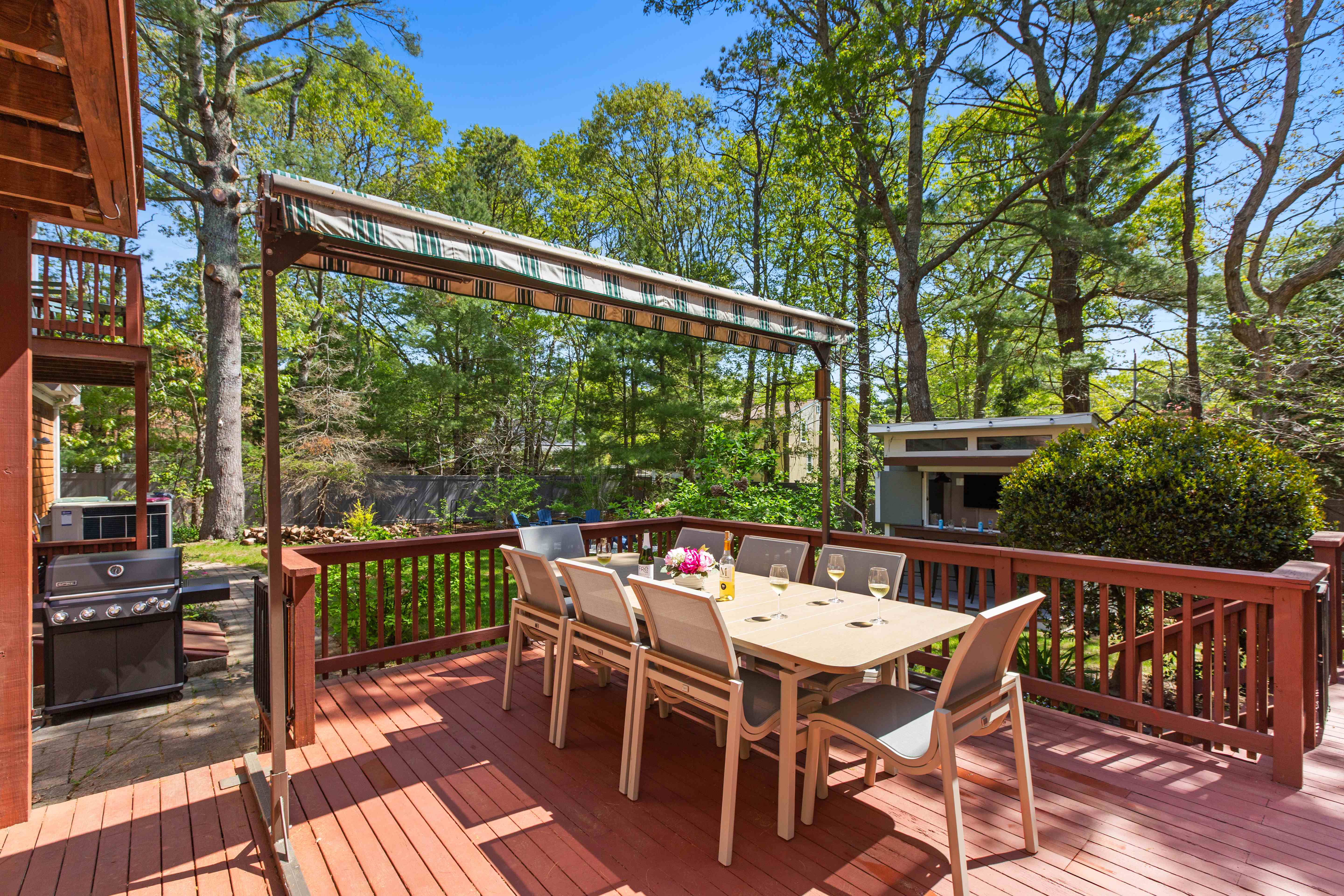 Deck dining set with a gas grill and the outdoor bar shed beyond