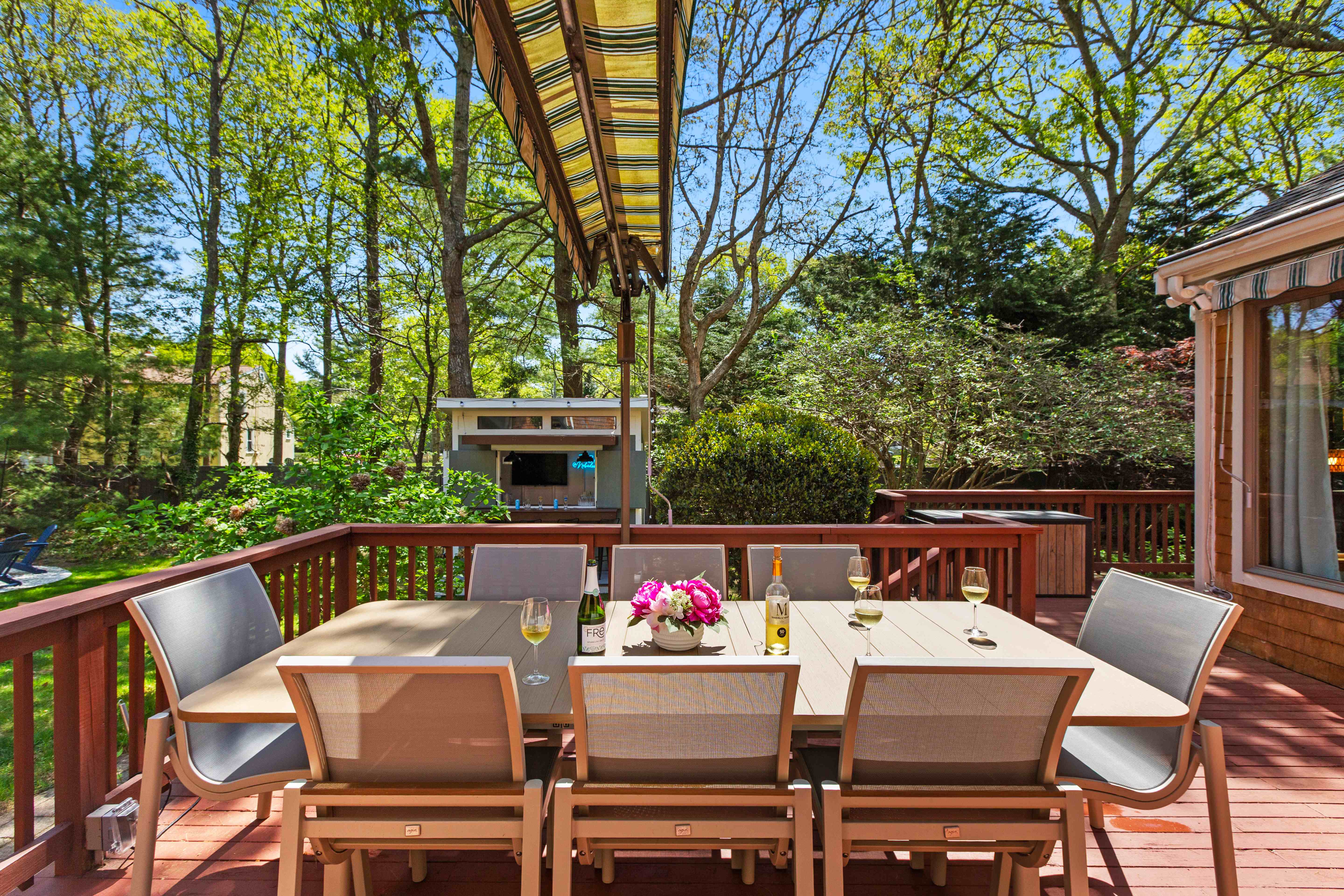 Sun-dappled deck dining table framed by tall backyard pines