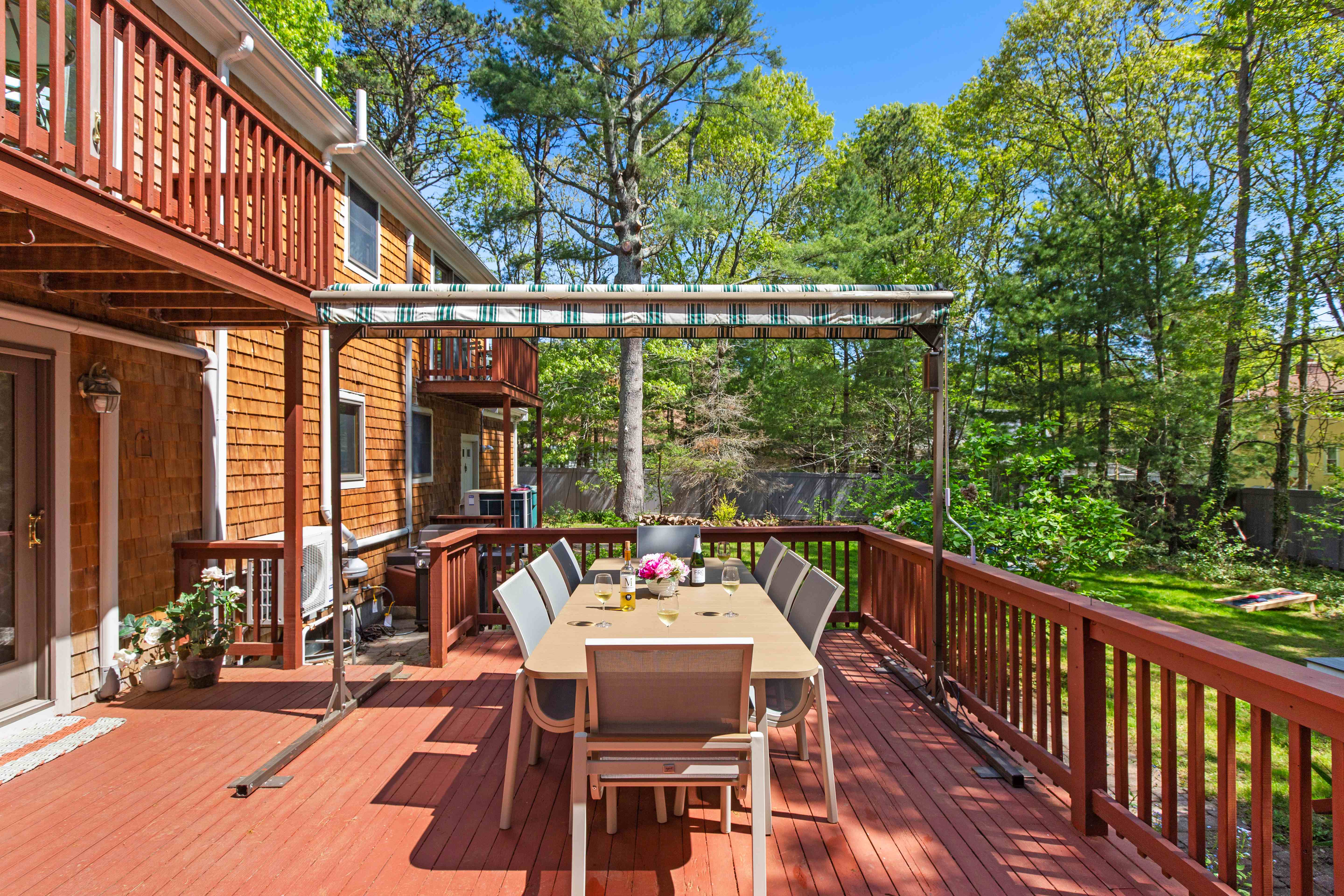 Angled view down the deck dining table toward the shingled house and grill