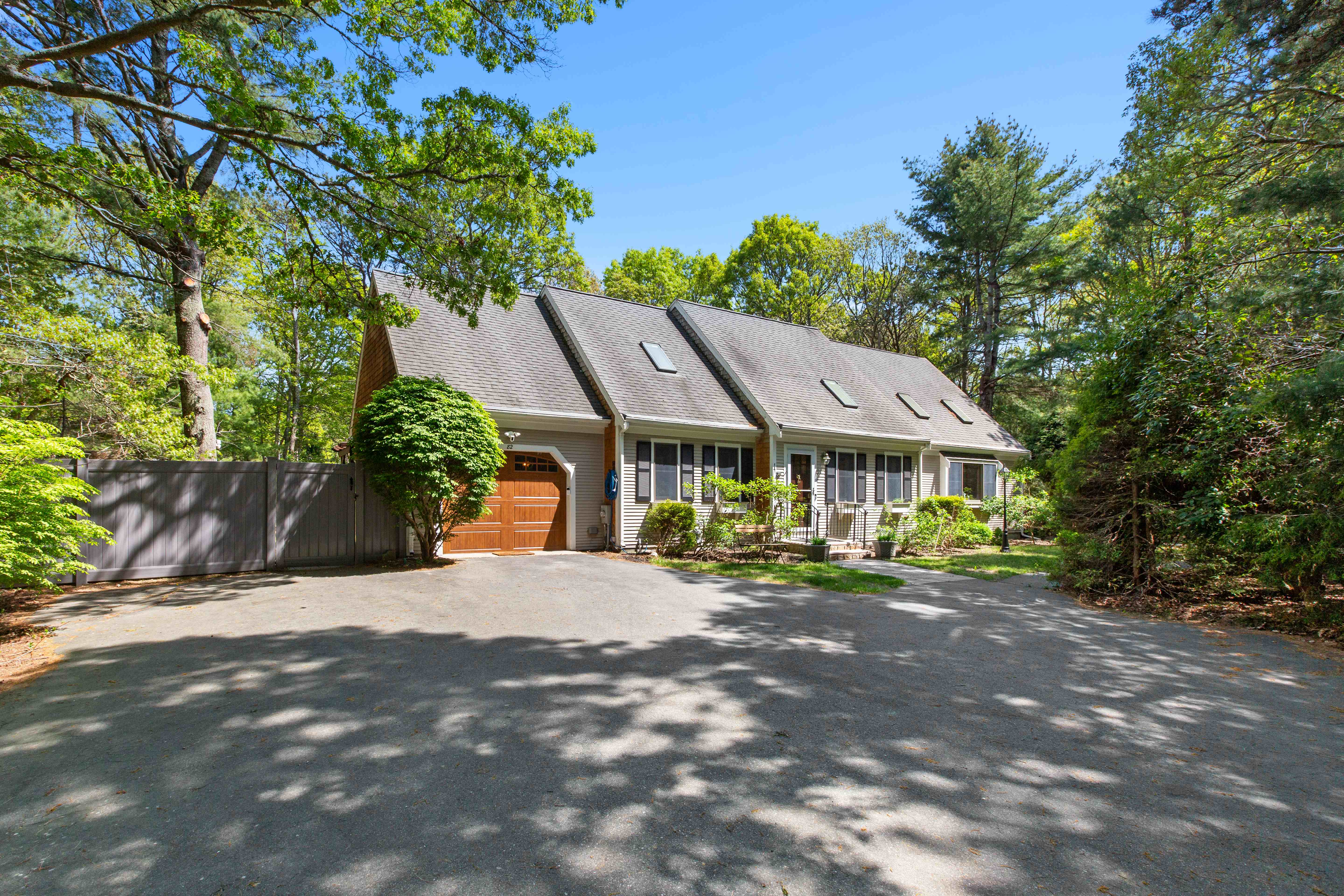 Front facade with a triple-gable roofline, wood garage door, and privacy fence framed by tall pines