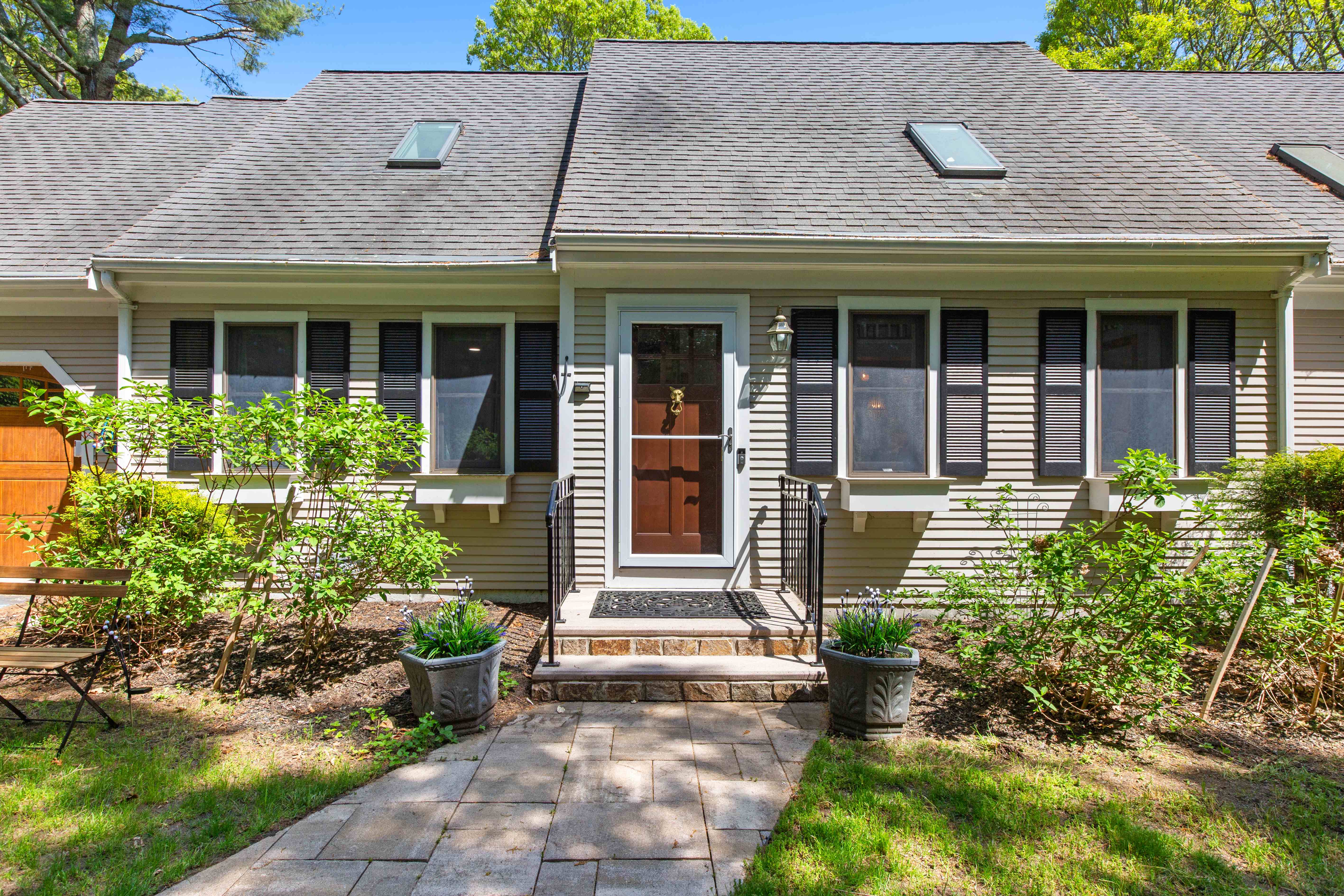 Covered front entry with a paneled door, brass knocker, black shutters, and potted lavender along the paver walkway