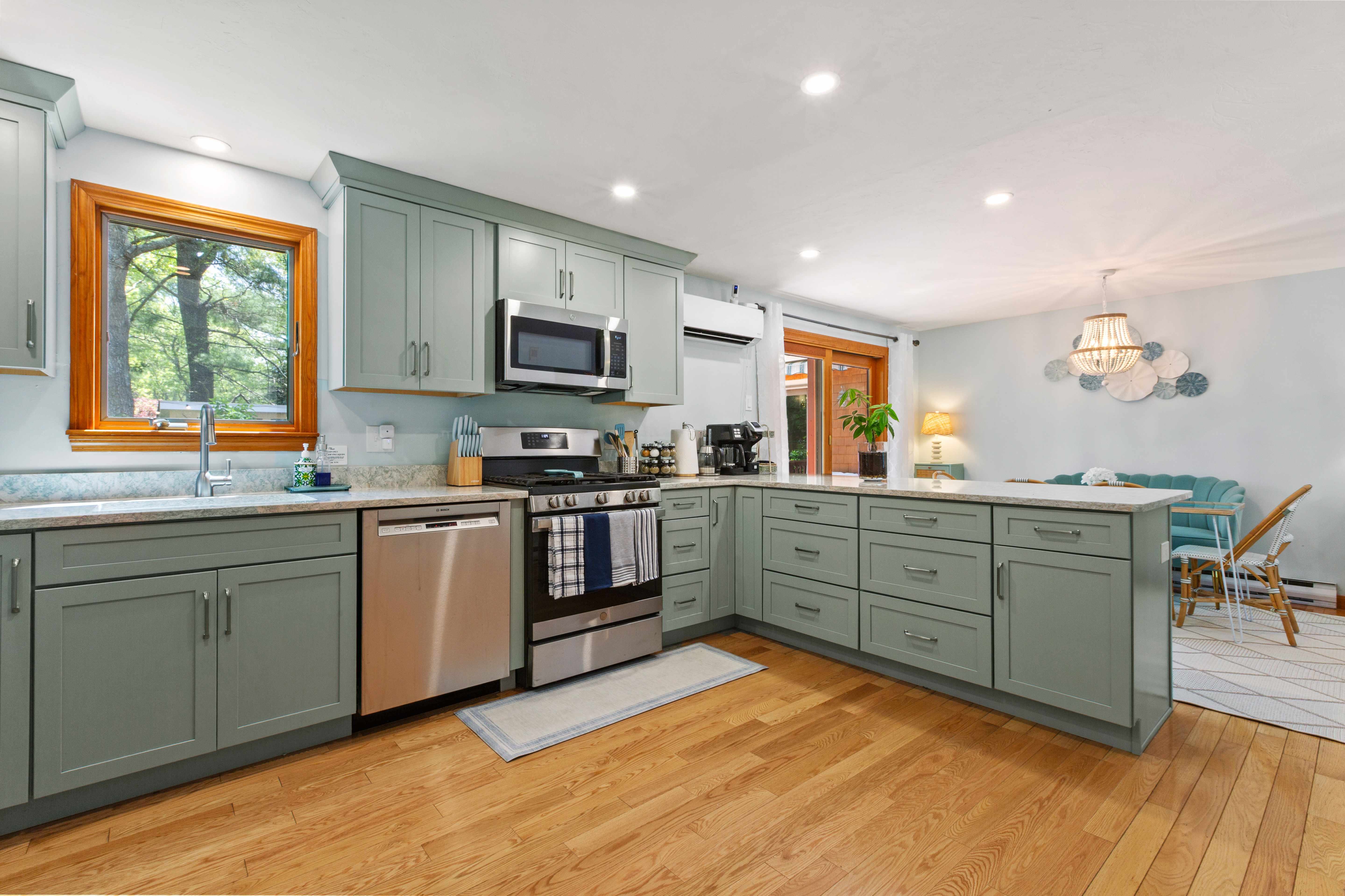 Sage-green kitchen with a gas range, dishwasher, and a marble peninsula opening to the dining nook with a teal banquette