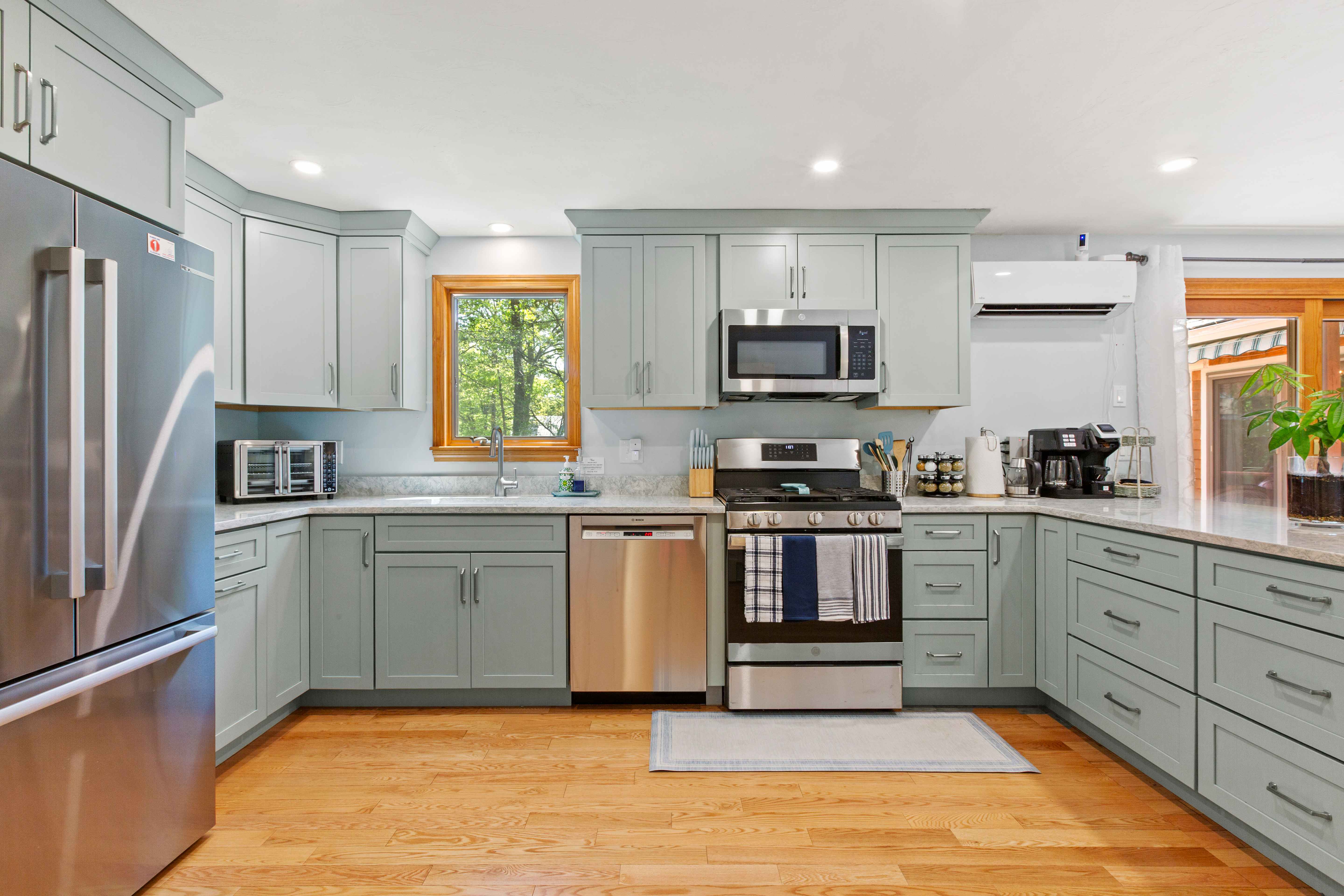 Straight-on view of the range wall with stainless microwave, a window over the sink, and sage shaker cabinetry