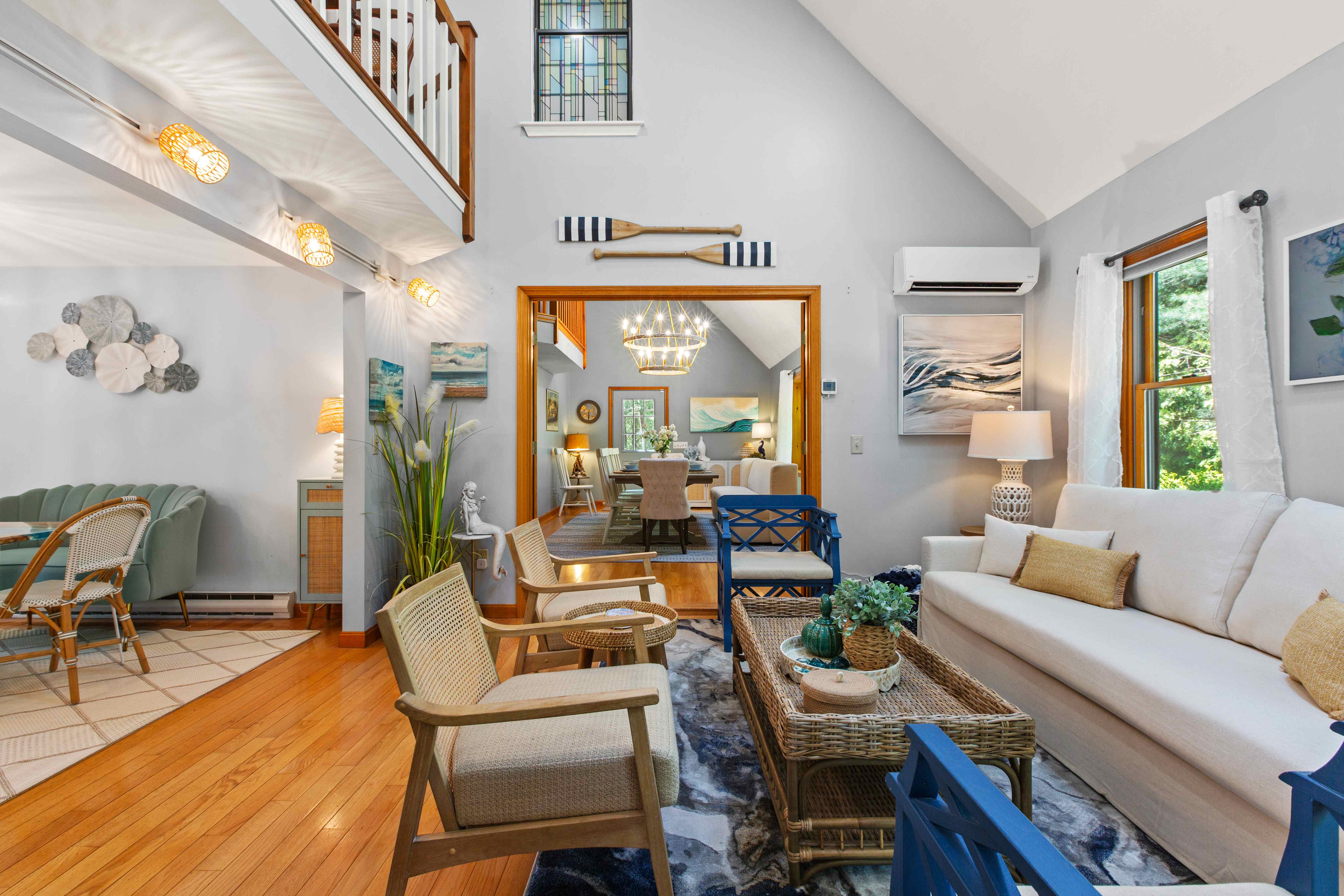 Vaulted great room with a cream sofa, blue fretwork chairs, and a wicker coffee table beneath a loft balcony and stained-glass window