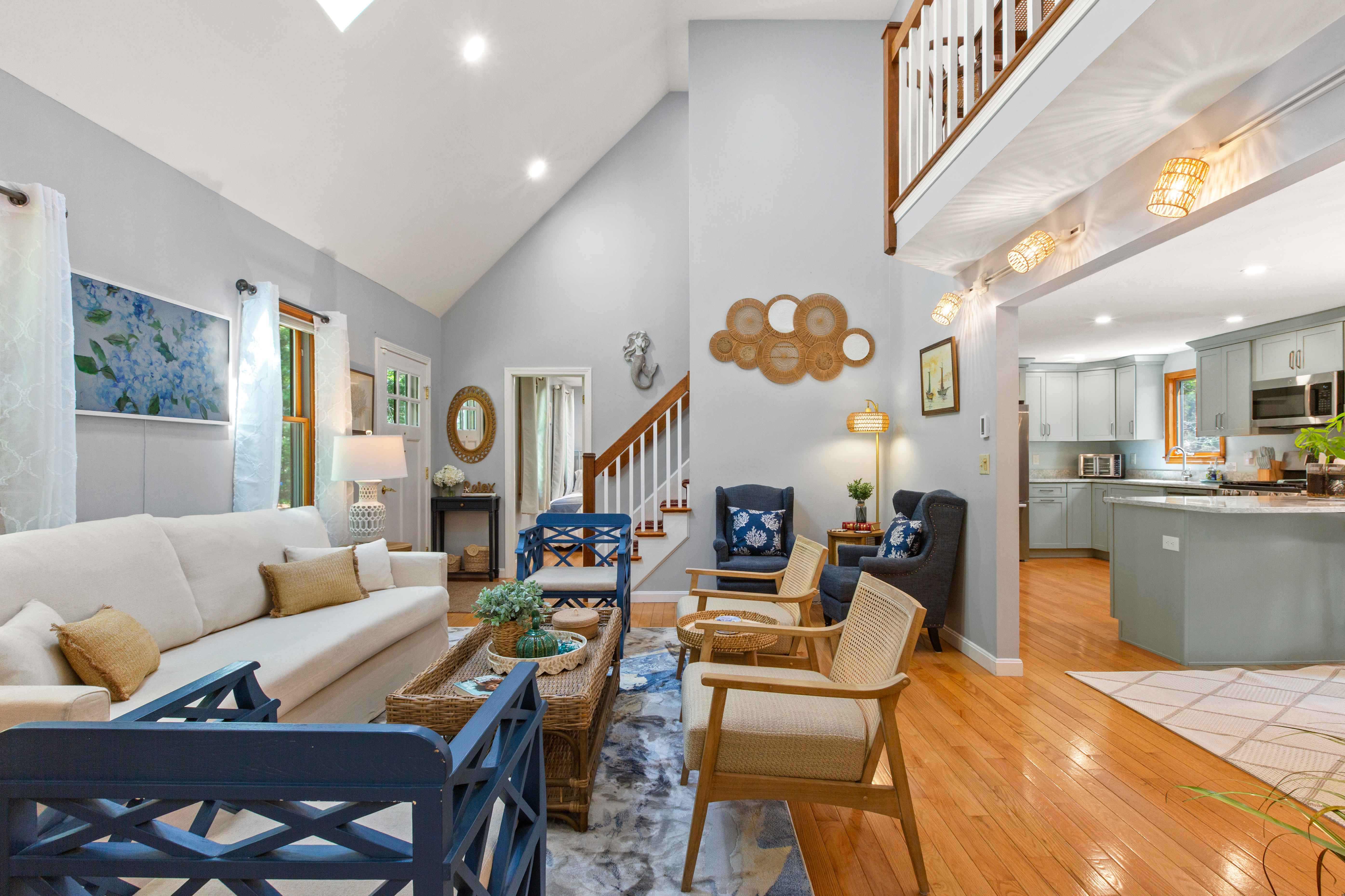 Living room opening to the kitchen, with a cream sofa, hydrangea painting, and staircase to the loft