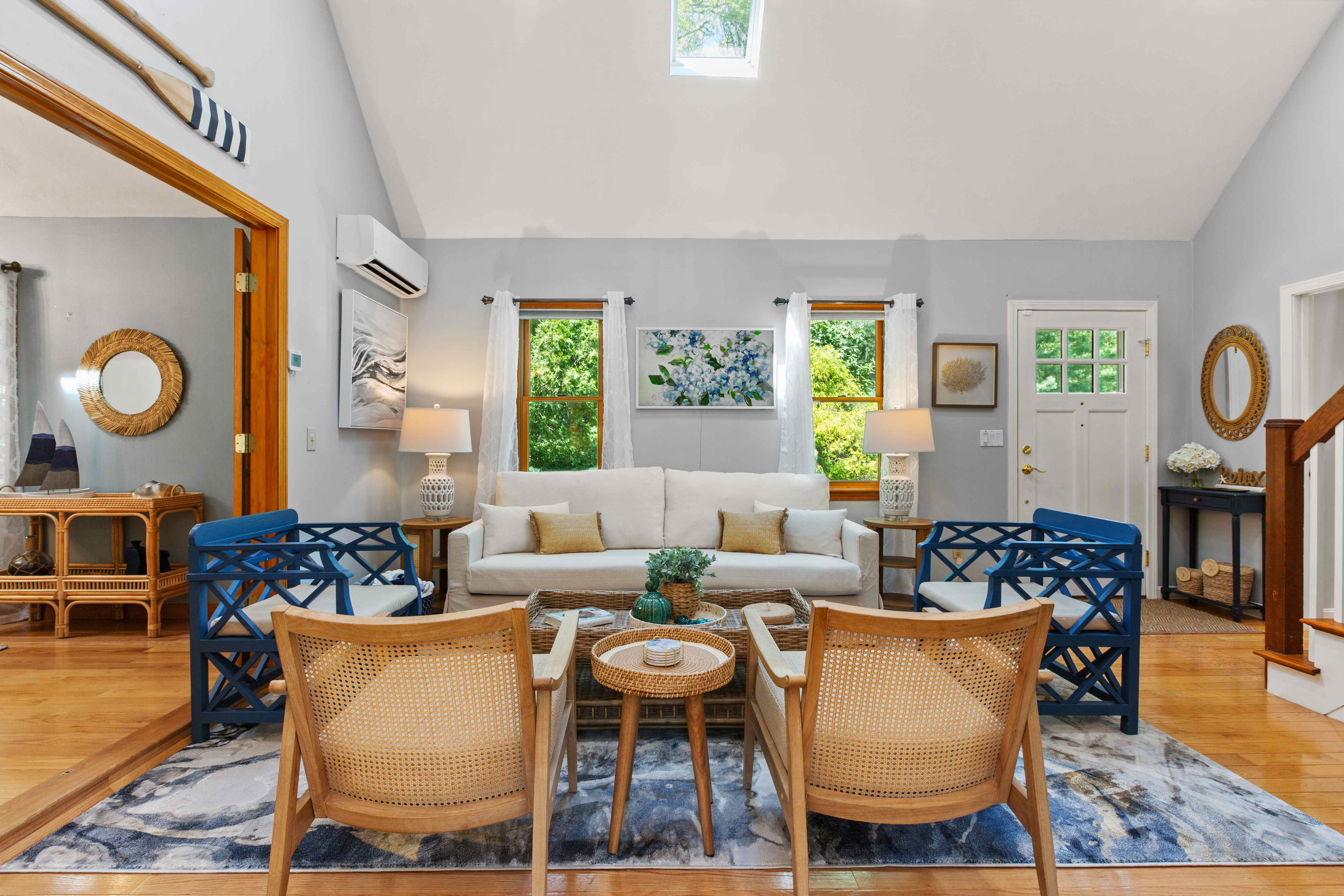 Symmetrical seating with a cream sofa between two windows, flanked by blue and cane accent chairs