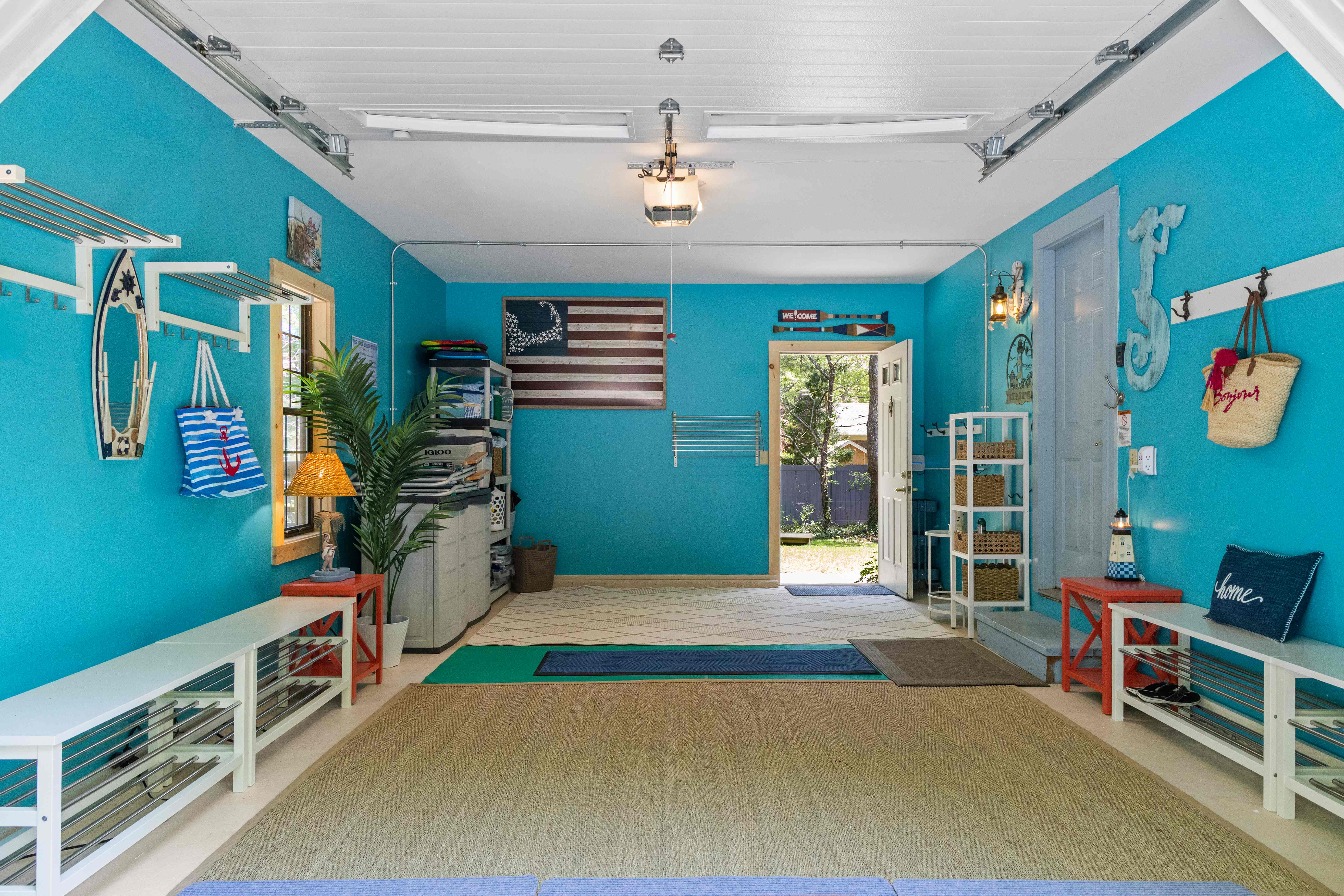 Turquoise mudroom with white shoe-rack benches along both walls, wall hooks, rustic American flag art, and the back door open to the wooded yard