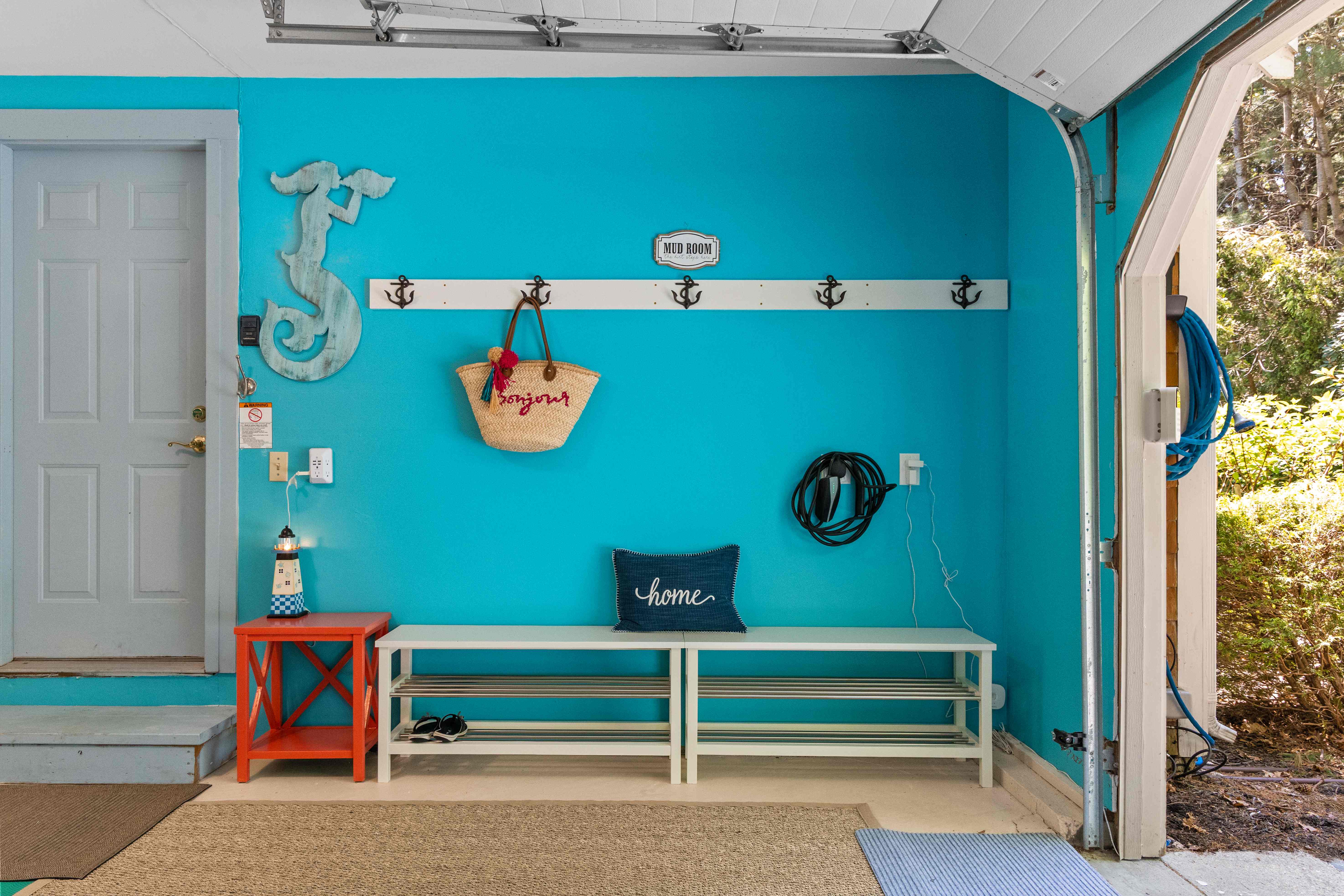 Mudroom wall with a "MUD ROOM" sign, a row of anchor coat hooks, a mermaid wall cutout, a white shoe bench, and a wall-mounted EV charger