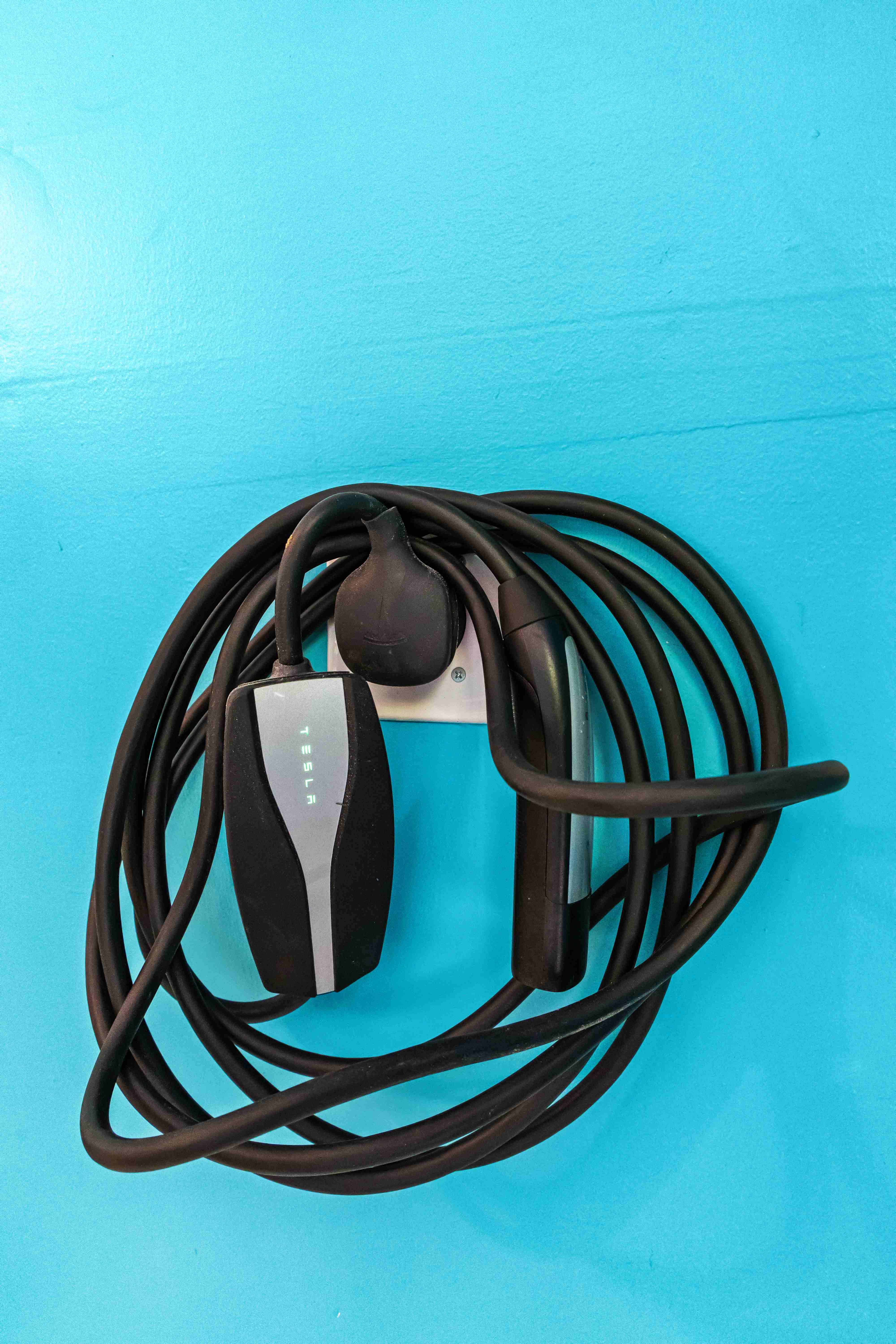 Coiled black Tesla Level 2 EV charger mounted on the turquoise mudroom wall