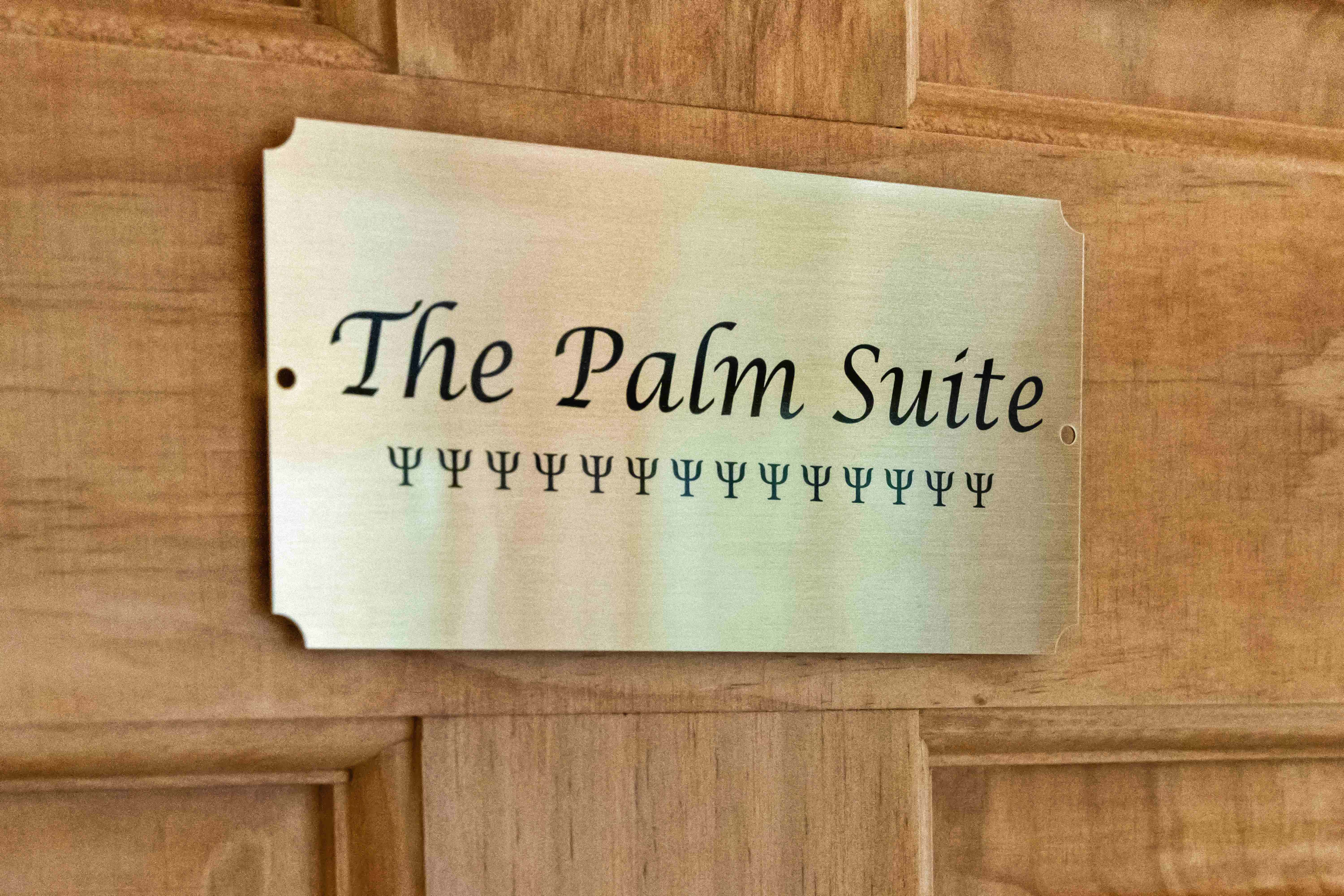 Brass door plaque reading "The Palm Suite" mounted on a wood-paneled door