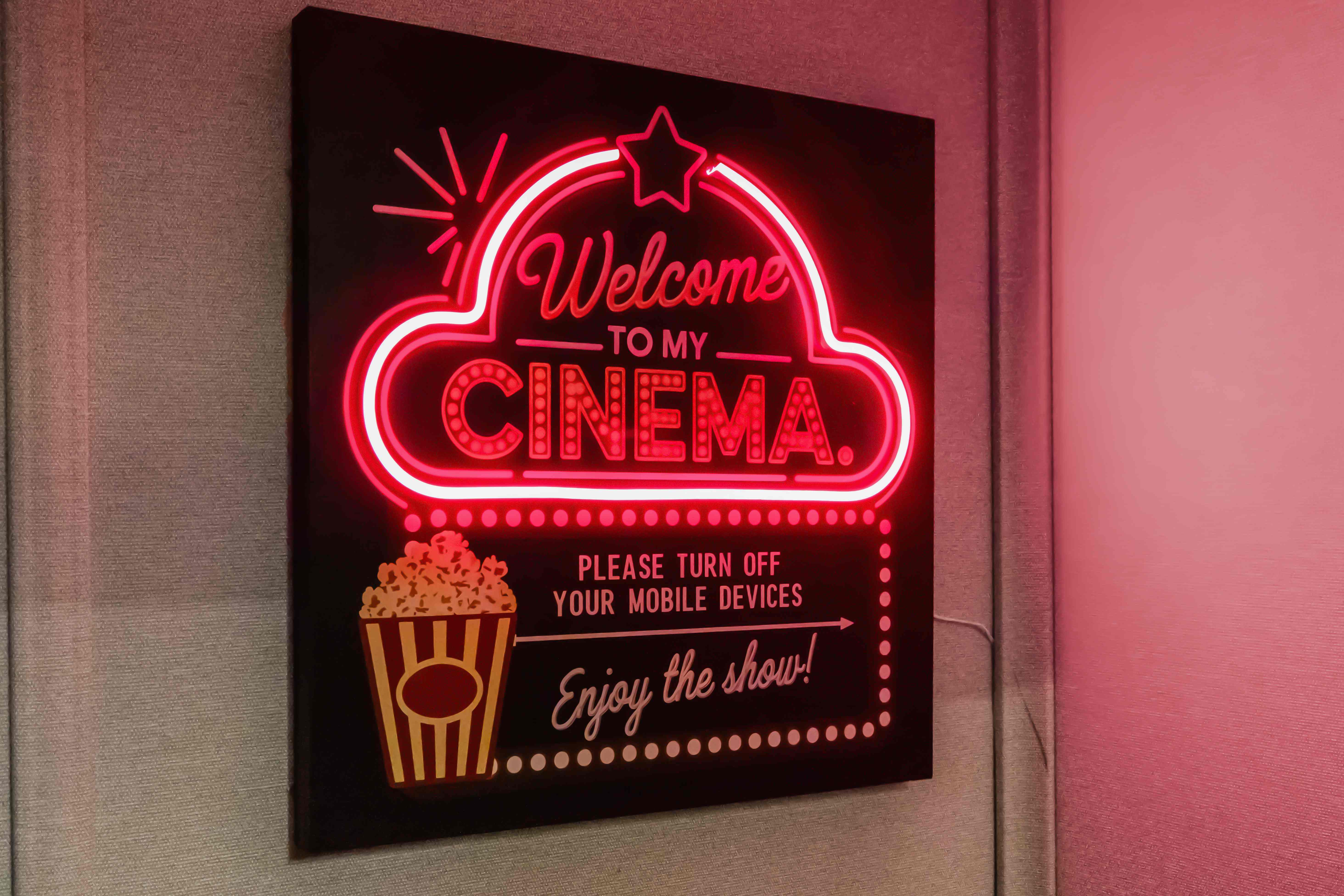 Red neon "Welcome to my Cinema" sign with popcorn and star artwork on the theater wall